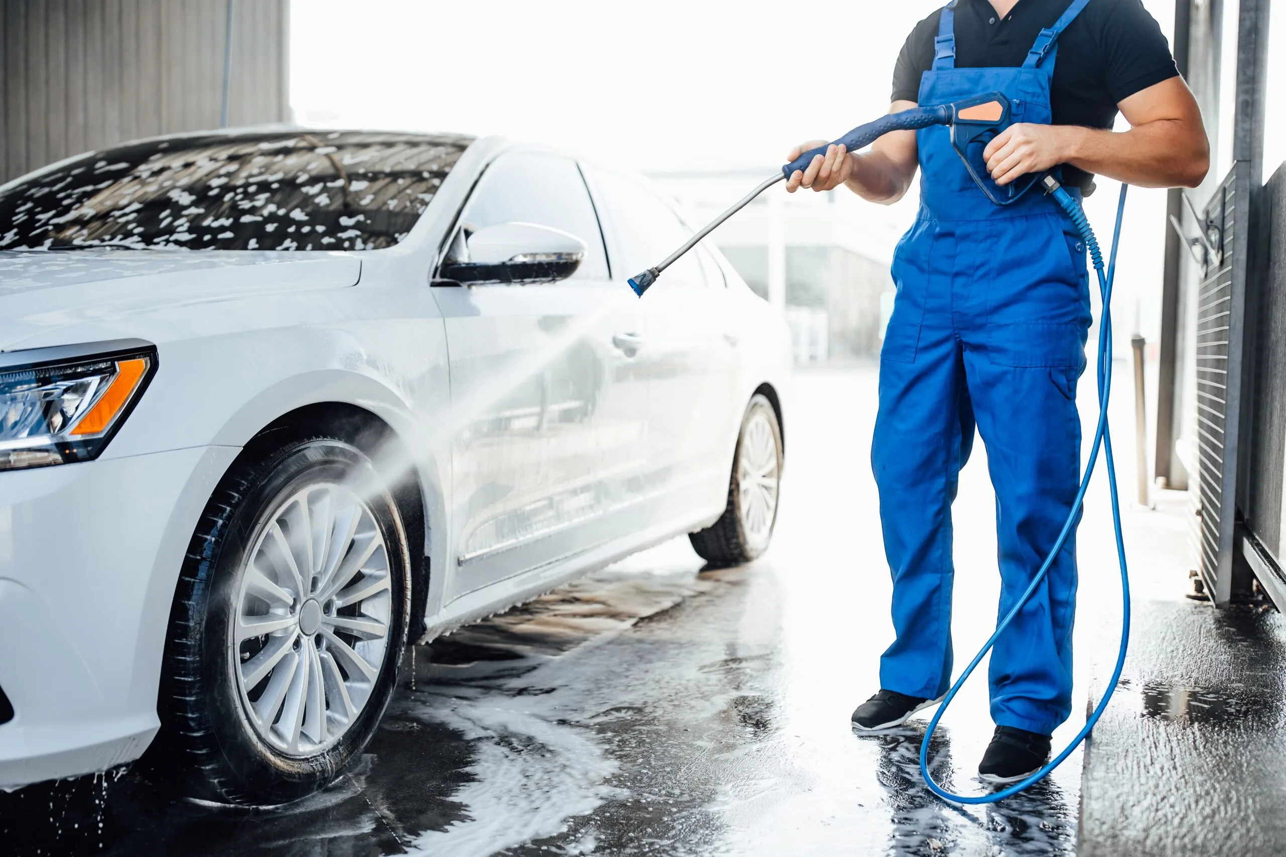 professional-washer-blue-uniform-washing-luxury-car-with-water-gun-open-air-car-wash-scaled
